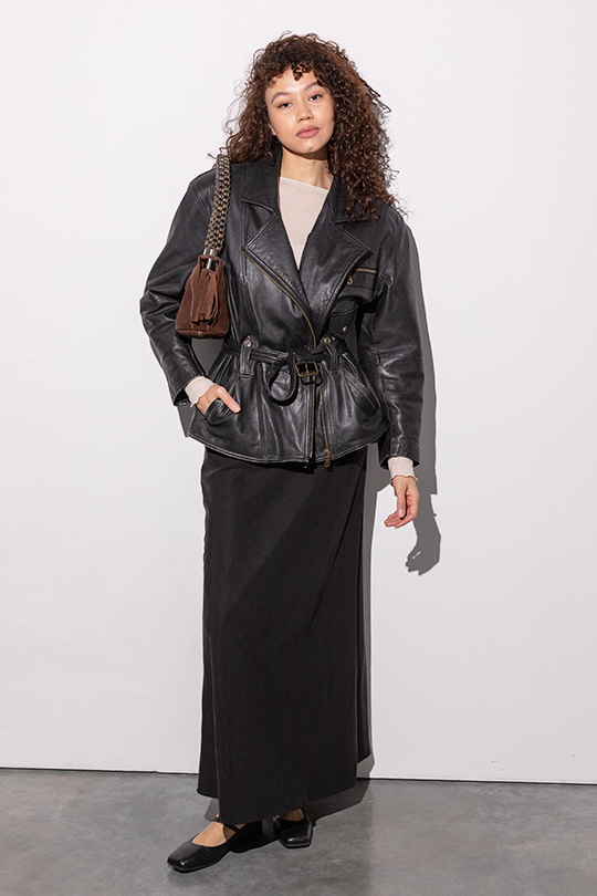 Кудрявая девушка в черной винтажной кожаной куртке и макси-юбке с балетками.